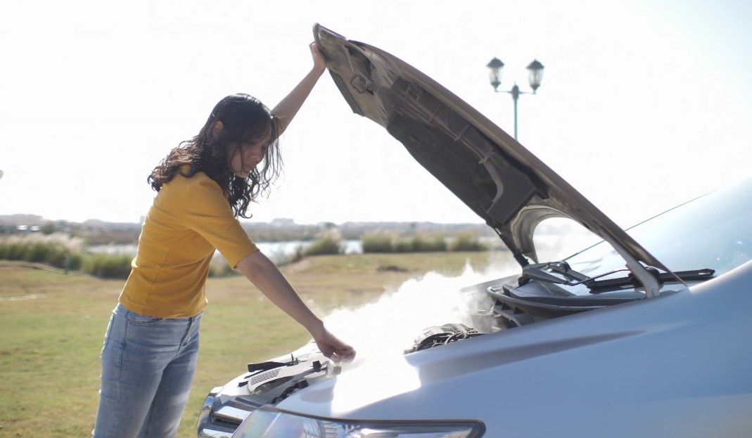 Žena proverava motor koji se puši ispod haube