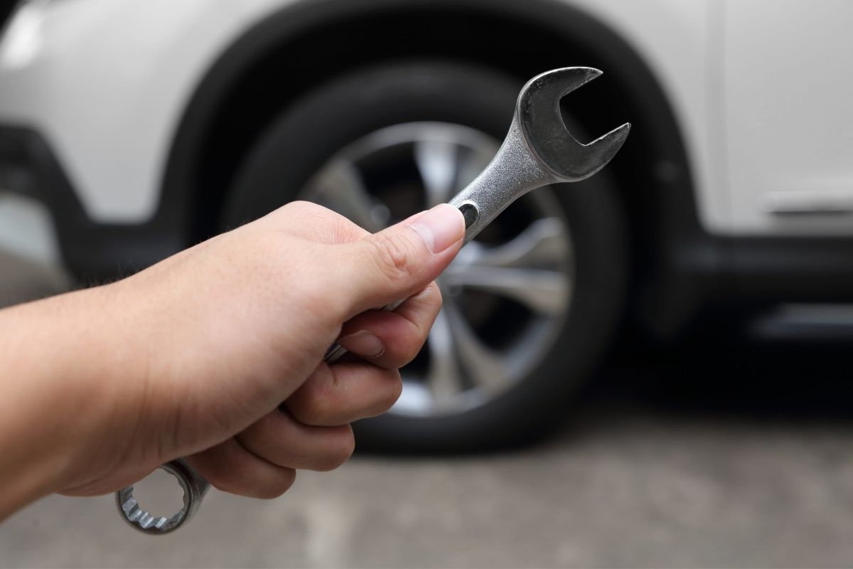 osoba drži ključ za popravljanje automobila, u pozadini automobil bele boje